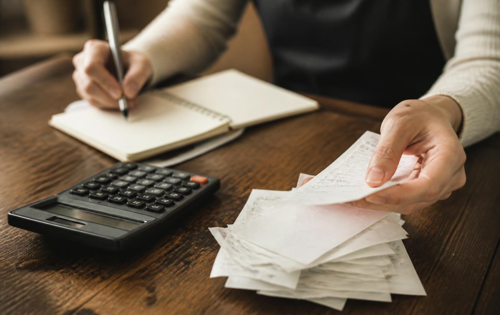 Hands sorting receipts beside a calculator on a wooden desk